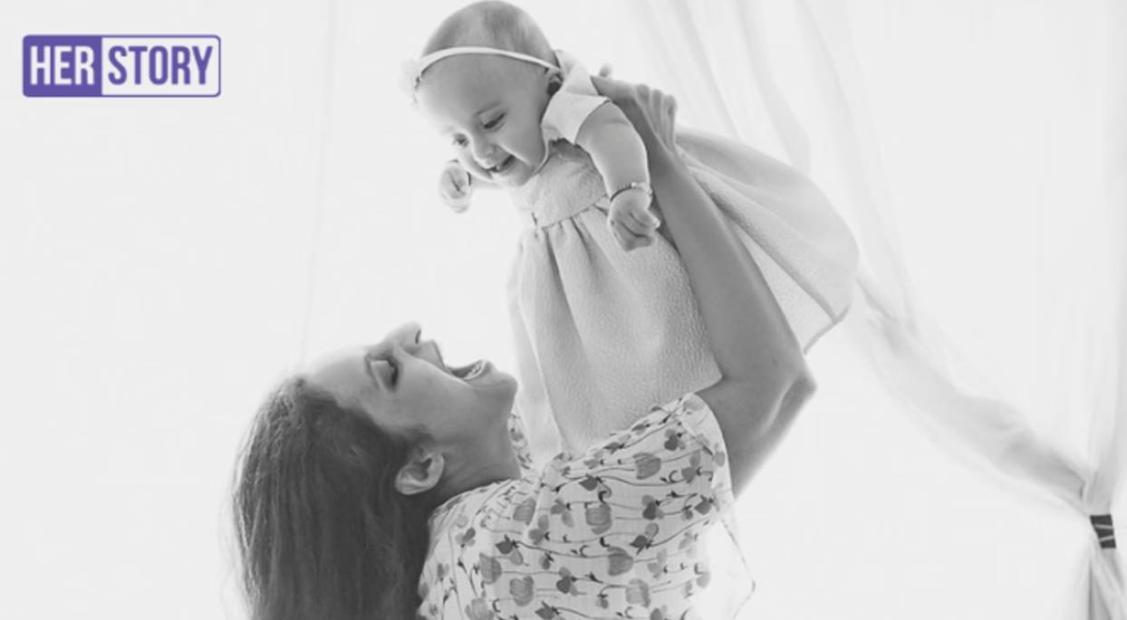 A joyful moment captured in black and white as a mother lifts her smiling infant daughter in the air, embodying the warmth of motherhood and the strength of a modern working woman.