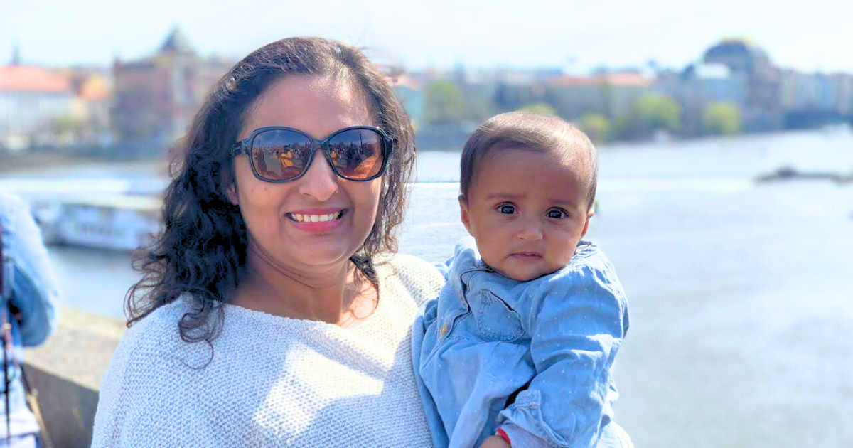 Smiling mother holding her baby while sightseeing by the river on a sunny day in Europe